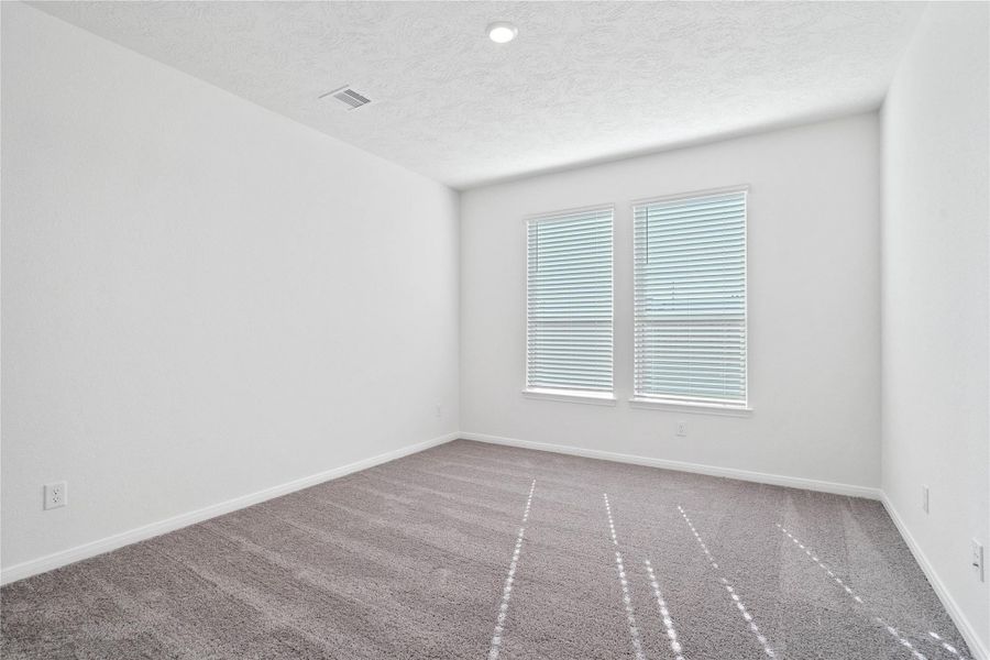 Relax and unwind after a long day in this impressive primary suite! This generously sized room offers plush carpeting, custom neutral paint, high ceilings, recessed lighting, and large windows with privacy blinds for added comfort and tranquility.