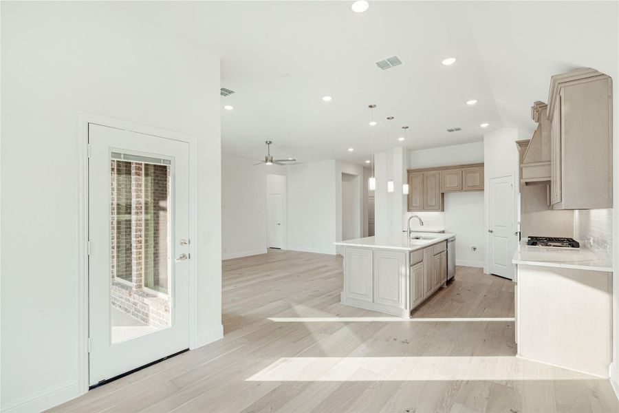 Open-concept kitchen with center island, tan cabinets, light hardwood floors, and view into living area