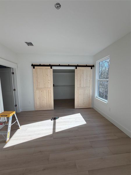 Unfurnished bedroom featuring a barn door, a spacious closet, and light wood-style flooring