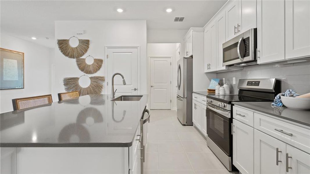 Kitchen with appliances with stainless steel finishes, dark countertops, a kitchen island with sink, recessed lighting, and white cabinets Kitchen with appliances with stainless steel finishes, dark countertops, a kitchen island with sink, recessed lighting, and white cabinets