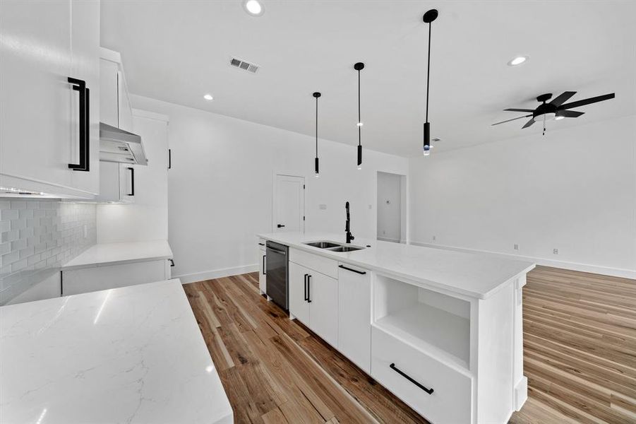 Kitchen featuring dishwasher, an island with sink, decorative light fixtures, white cabinets, and light hardwood / wood-style floors