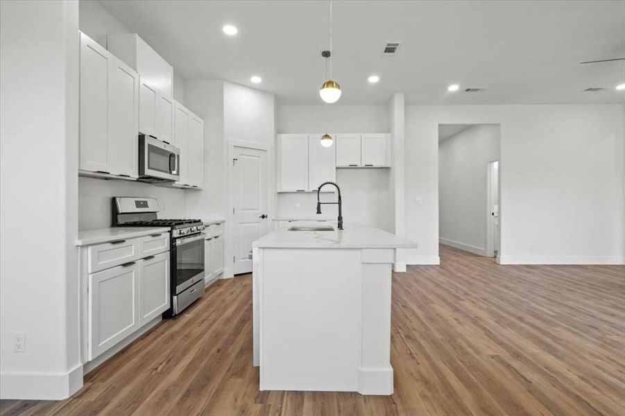 Kitchen with appliances with stainless steel finishes, hanging light fixtures, white cabinets, recessed lighting, and light wood-style flooring