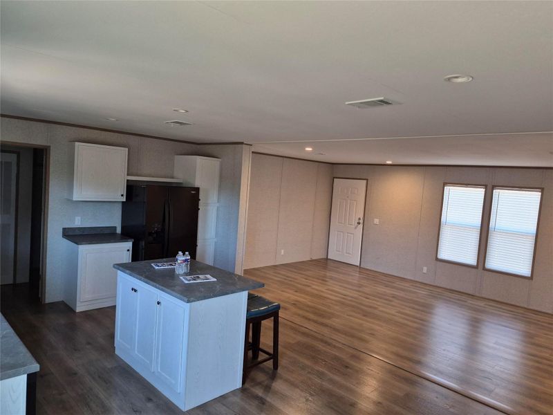 Kitchen featuring white cabinets, dark countertops, black refrigerator with ice dispenser, a kitchen breakfast bar, and a kitchen island