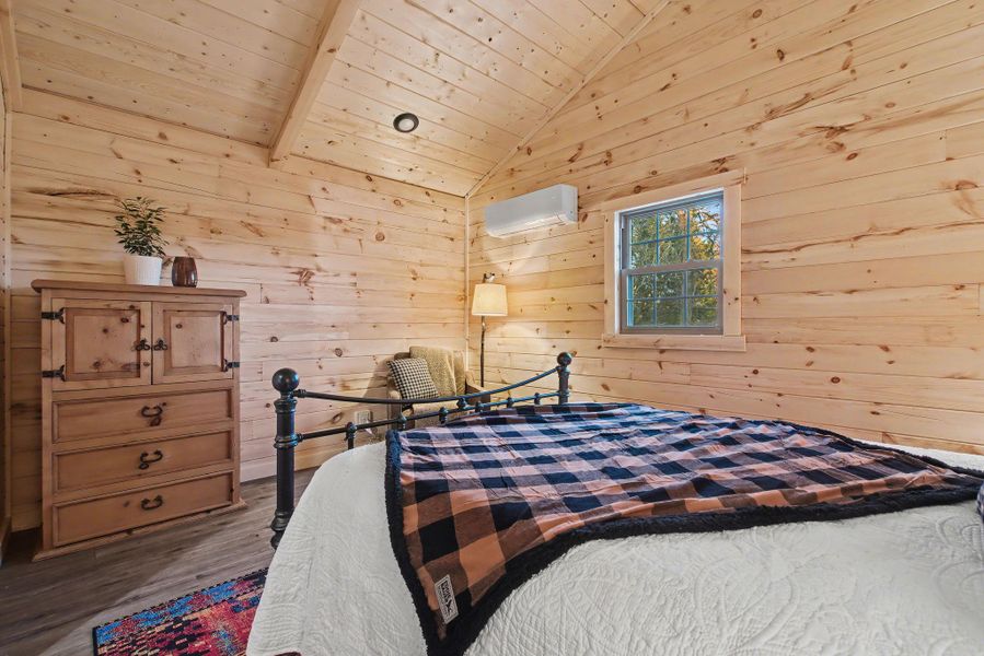 Bedroom featuring wood walls, lofted ceiling, wood finished floors, a wall unit AC, and wooden ceiling