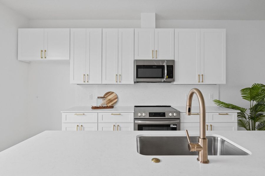Contemporary kitchen featuring white cabinetry with gold-tone hardware, stainless steel appliances, a white tile backsplash, and a large sink with a gold-tone faucet