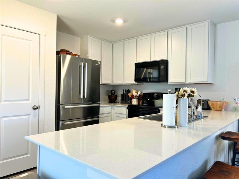 Kitchen featuring a kitchen bar, appliances, white cabinets, a peninsula, and light stone countertops Kitchen featuring a kitchen bar, appliances, white cabinets, a peninsula, and light stone countertops
