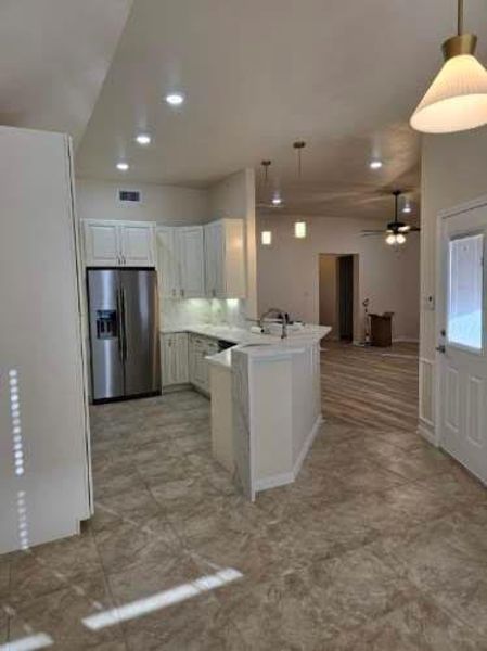 Kitchen featuring a peninsula, stainless steel fridge, decorative light fixtures, white cabinets, and ceiling fan Kitchen featuring a peninsula, stainless steel fridge, decorative light fixtures, white cabinets, and ceiling fan