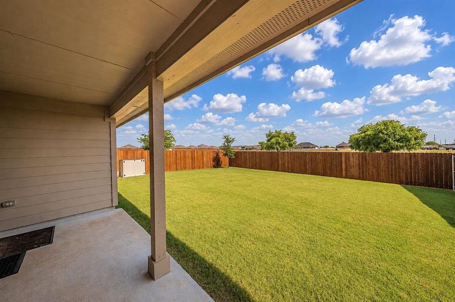Expansive backyard featuring a manicured lawn, full privacy fencing, and a covered concrete patio