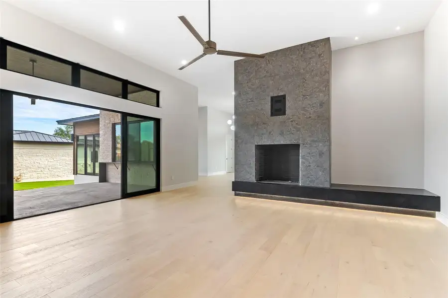 Unfurnished living room with a towering ceiling, a ceiling fan, wood finished floors, a tile fireplace, and recessed lighting Unfurnished living room with a towering ceiling, a ceiling fan, wood finished floors, a tile fireplace, and recessed lighting