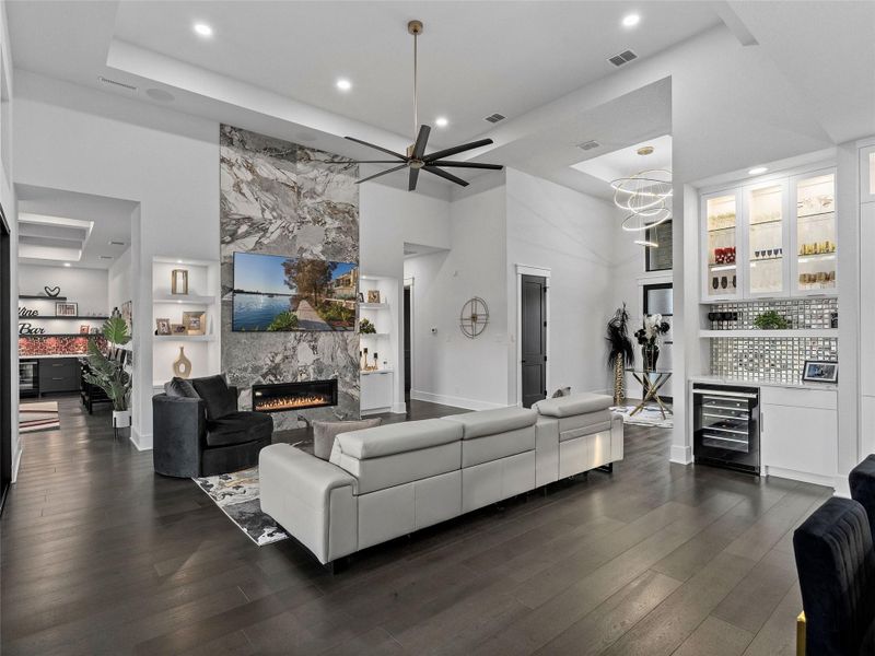 Living area with a dry bar, wine cooler, dark wood-type flooring, a fireplace, and a ceiling fan