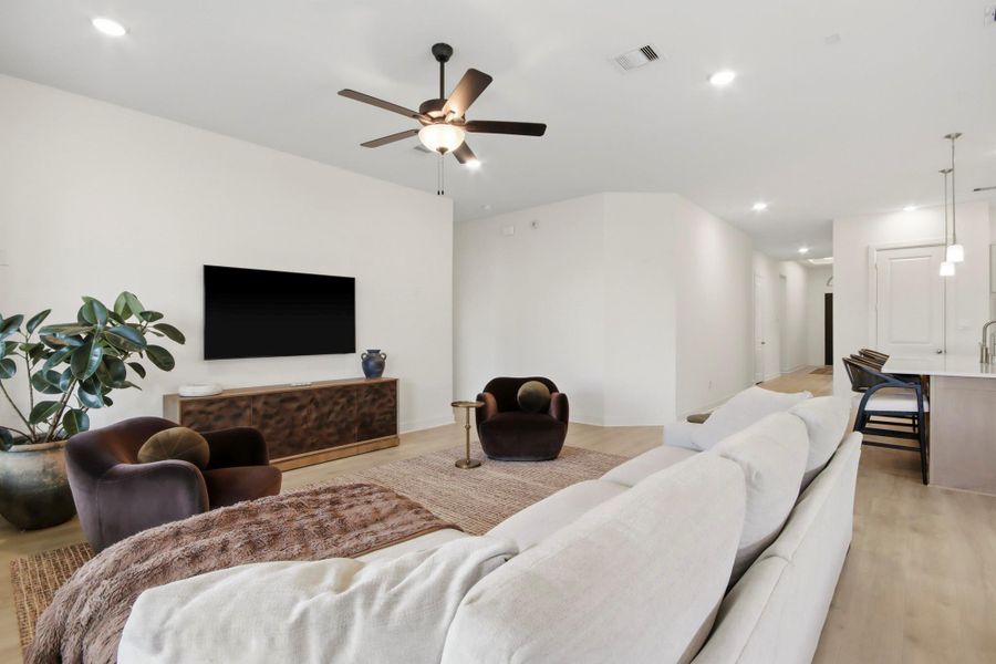 A contemporary living area with a comfortable seating space, streamlined media console, and stylish ceiling fan, flowing effortlessly into the bright kitchen and dining areas.
