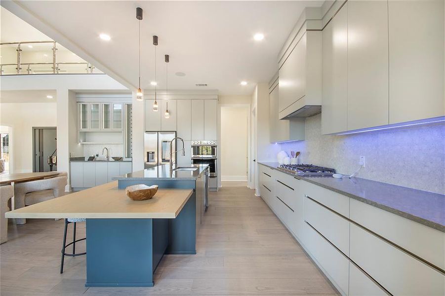 Kitchen featuring modern cabinets, a center island with sink, decorative light fixtures, appliances with stainless steel finishes, and a kitchen bar Kitchen featuring modern cabinets, a center island with sink, decorative light fixtures, appliances with stainless steel finishes, and a kitchen bar