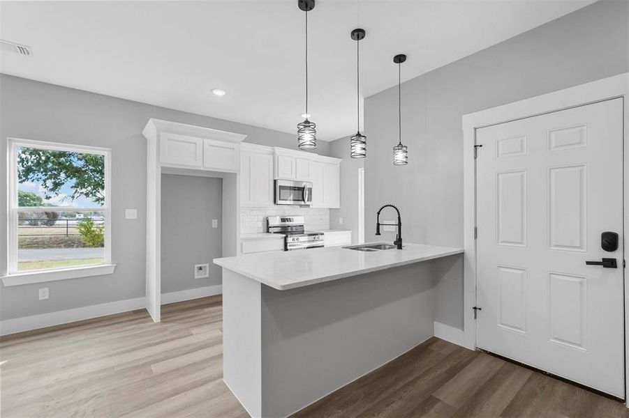 Kitchen featuring sink, decorative light fixtures, light hardwood / wood-style flooring, white cabinetry, and appliances with stainless steel finishes