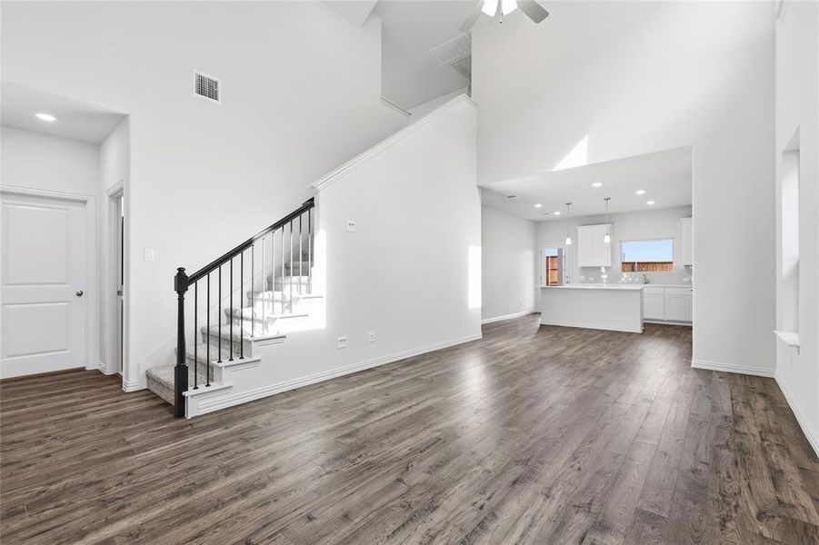 Spacious living area featuring wood-finish flooring, a contemporary staircase with black wrought iron spindles, and high ceilings