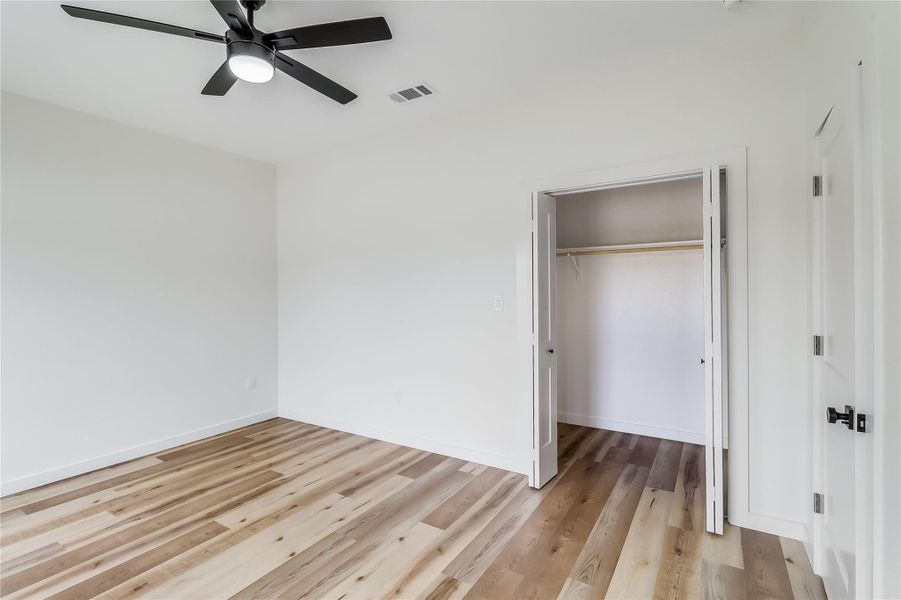 Unfurnished bedroom featuring a closet, light wood-type flooring, ceiling fan, baseboards, and visible vents