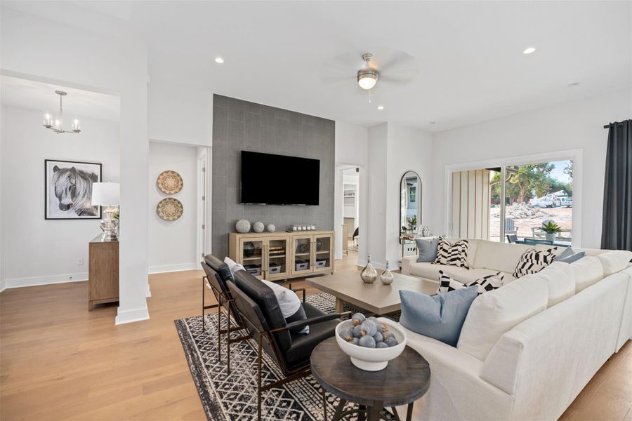Living room featuring a ceiling fan, light wood-style floors, recessed lighting, a chandelier, and an accent wall. The photos shown are of a completed home with the same floor plan and may not reflect the exact finishes, features, or layout of the home currently under construction.