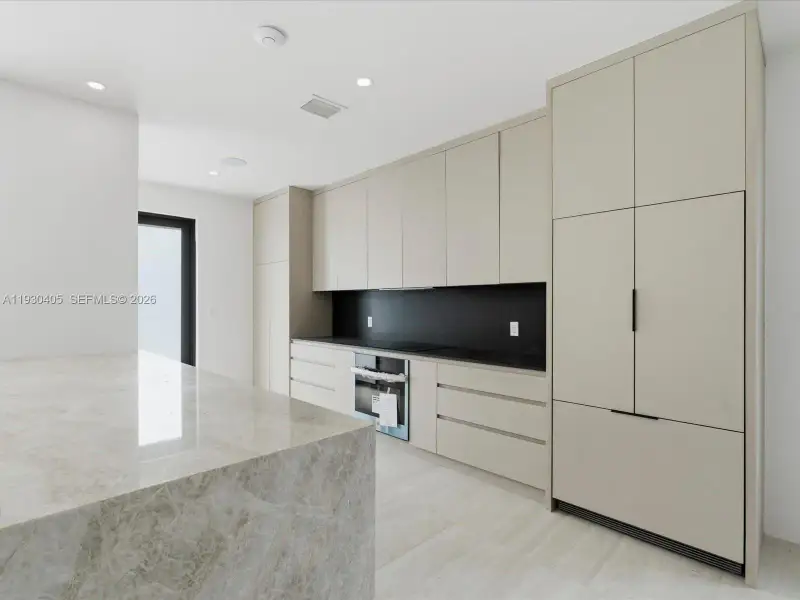 Kitchen featuring floor-to-ceiling cabinetry, a stone-top waterfall island, contrasting black backsplash, integrated appliances, and recessed lighting Kitchen featuring floor-to-ceiling cabinetry, a stone-top waterfall island, contrasting black backsplash, integrated appliances, and recessed lighting