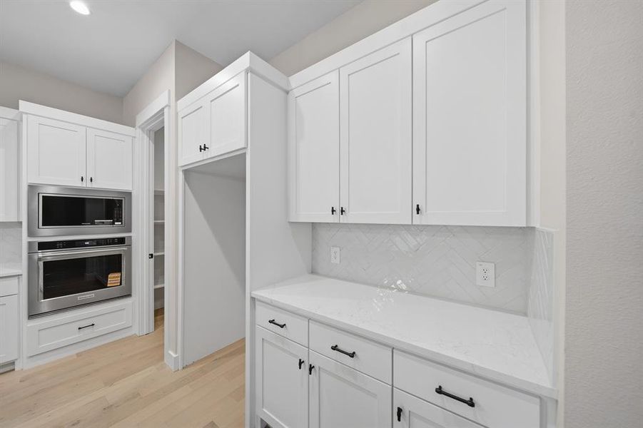 Kitchen featuring stainless steel appliances, white cabinets, light stone countertops, light wood-style floors, and backsplash