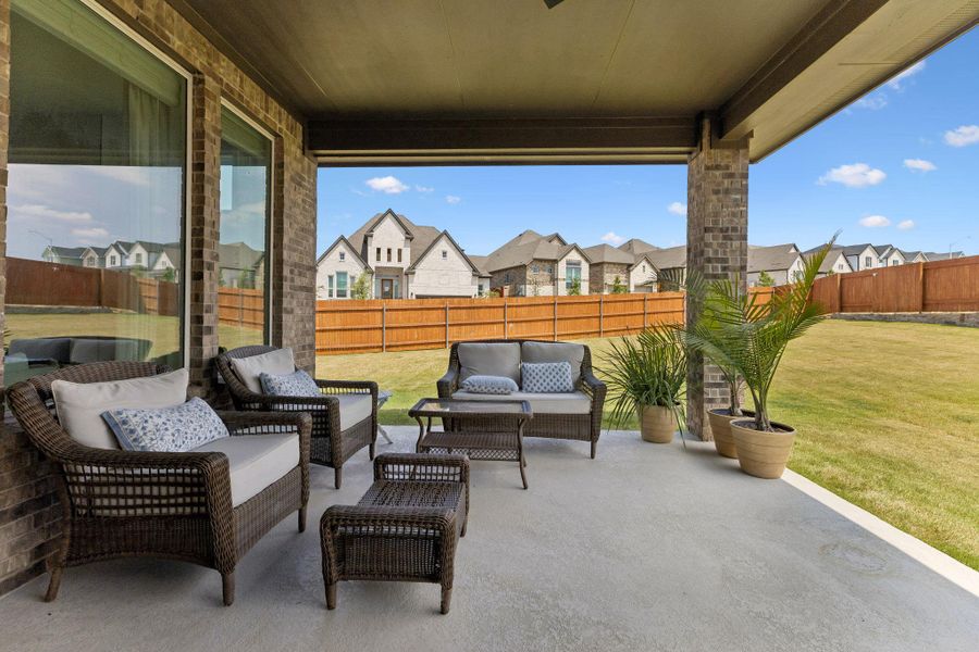 An inviting covered patio features concrete flooring and brick pillars overlooking a fenced lawn.