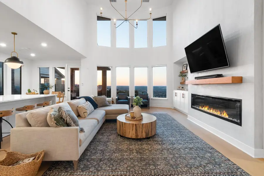 Great room with high ceilings, featuring a linear electric fireplace with a wood mantel, built-in cabinetry, and large windows Great room with high ceilings, featuring a linear electric fireplace with a wood mantel, built-in cabinetry, and large windows