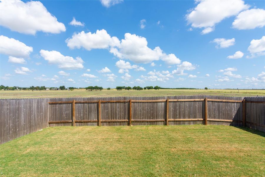 Expansive backyard featuring a wood privacy fence and a manicured lawn, bordered by open fields and distant trees
