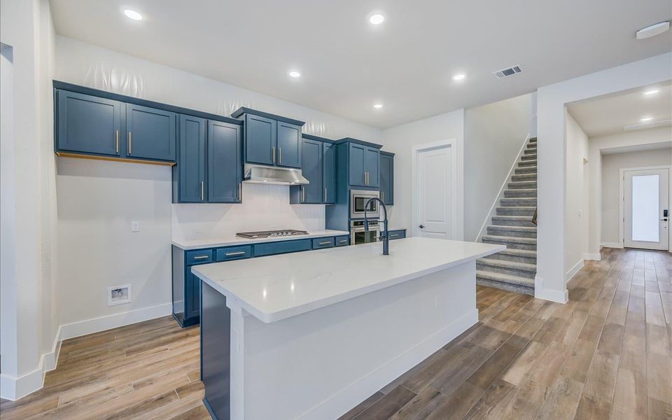 Kitchen with an island with sink, light wood-type flooring, recessed lighting, blue cabinetry, and stainless steel appliances
