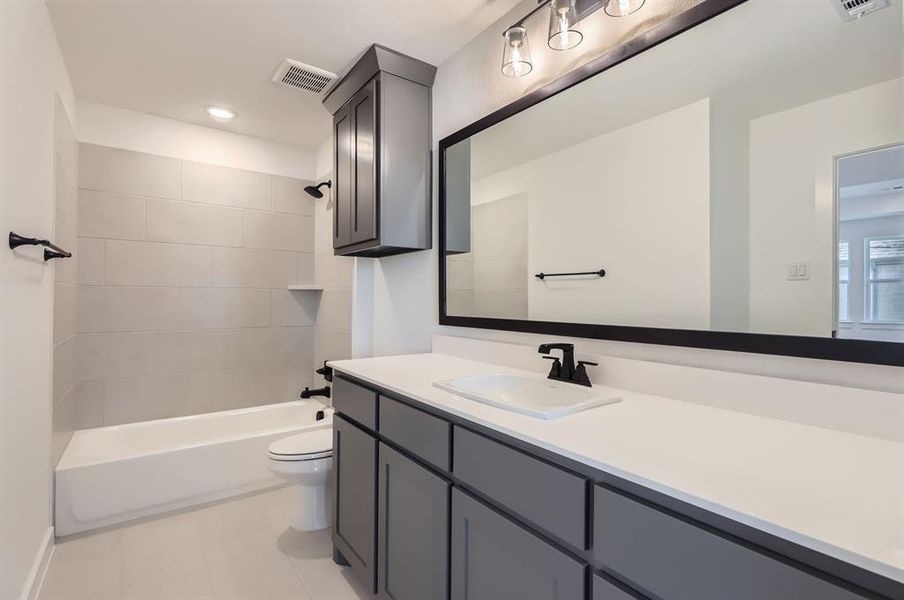 Full bathroom with toilet, tiled shower / bath combo, vanity, and tile patterned floors