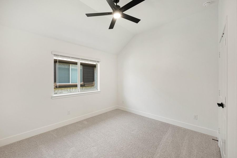 Empty bedroom with vaulted ceiling, black ceiling fan, carpet flooring, and single window
