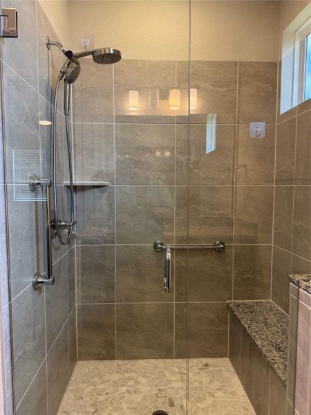 A spacious, glass-enclosed shower boasts a built-in bench and modern tile.