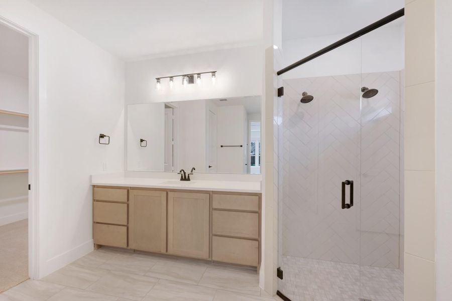 Bathroom with wood vanity, large mirror, and glass-enclosed tile shower with black hardware