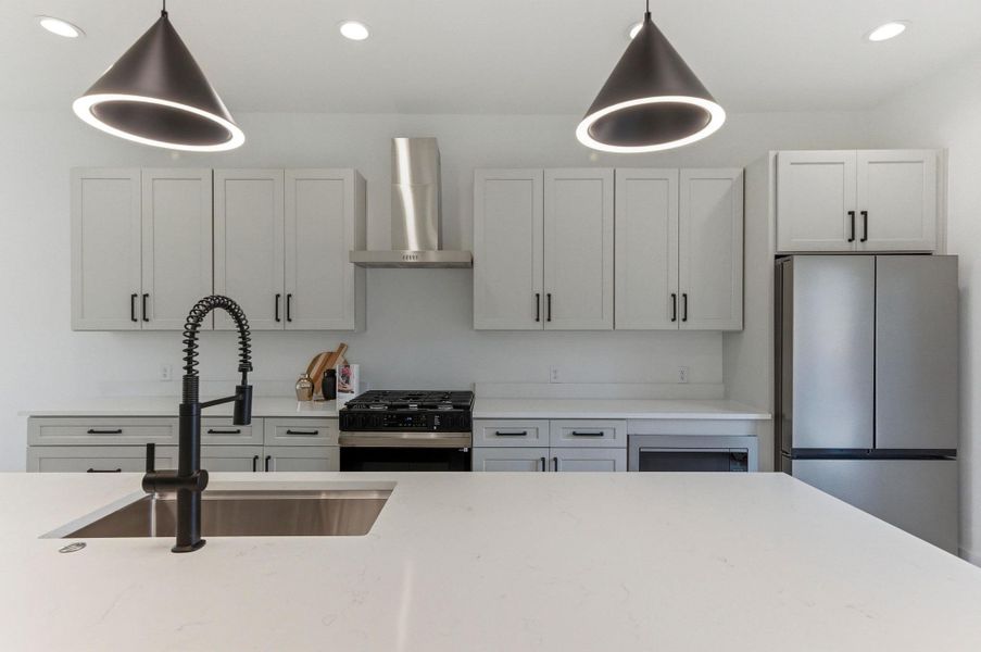 Kitchen with freestanding refrigerator, gas stove, wall chimney exhaust hood, recessed lighting, and light stone countertops