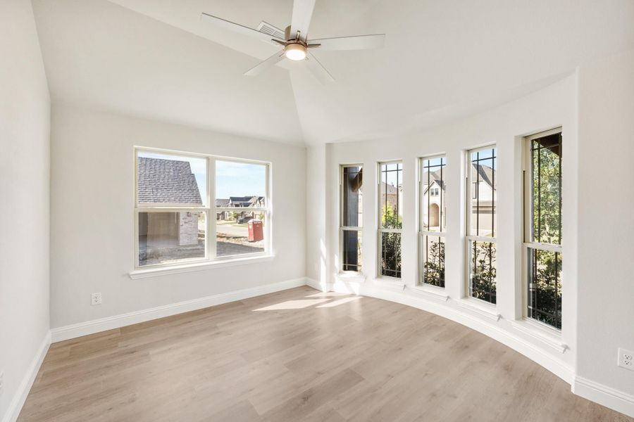 Empty room with vaulted ceiling, ceiling fan, light wood floors, and large windows on two walls Empty room with vaulted ceiling, ceiling fan, light wood floors, and large windows on two walls
