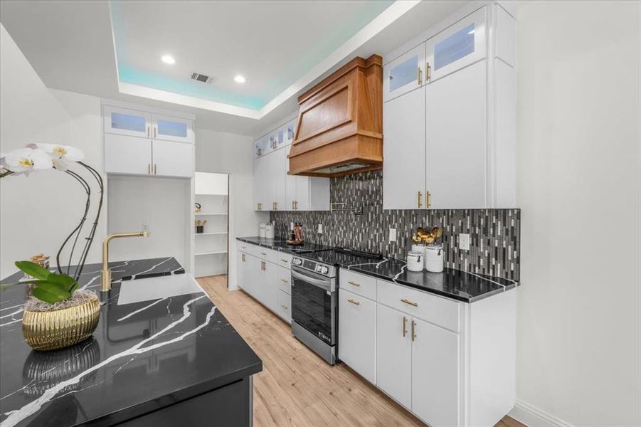 Kitchen with glass insert cabinets, white cabinets, light wood-type flooring, stainless steel electric stove, and recessed lighting