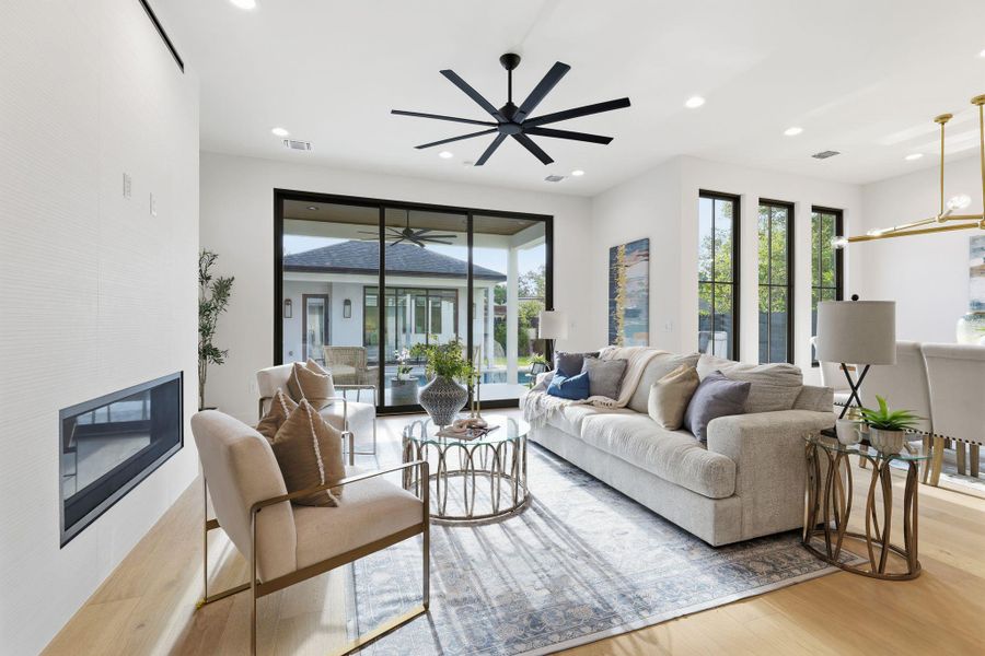Living room with a glass covered fireplace, a ceiling fan, light wood-type flooring, and recessed lighting