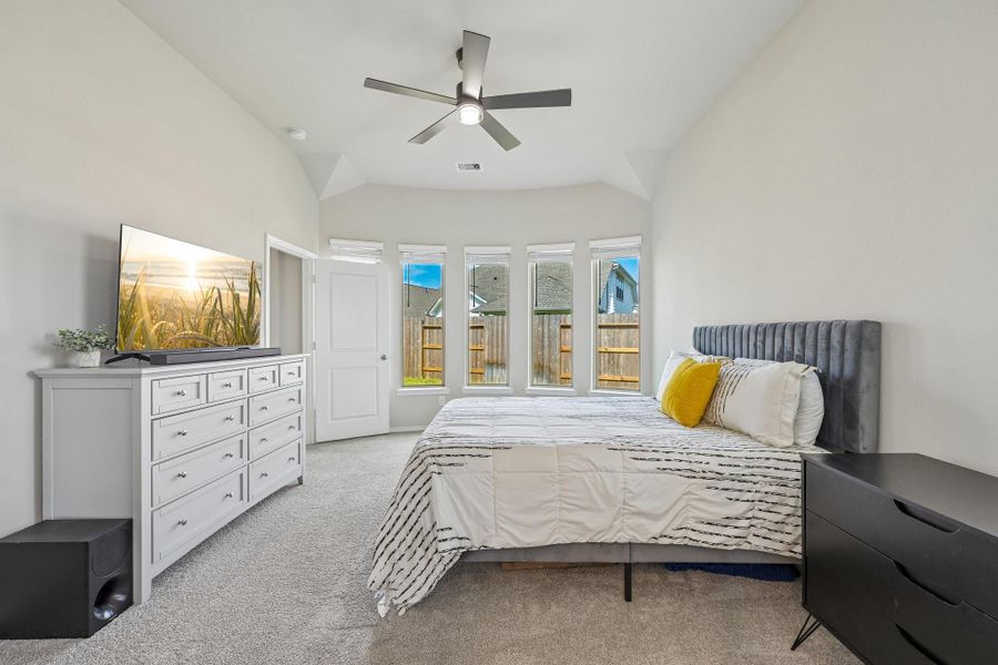 Spacious bedroom featuring a cozy bed, ceiling fan, and abundant natural light from multiple windows overlooking the backyard.