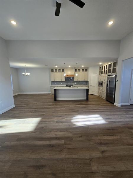 Unfurnished living room featuring ceiling fan with notable chandelier and dark hardwood / wood-style floors