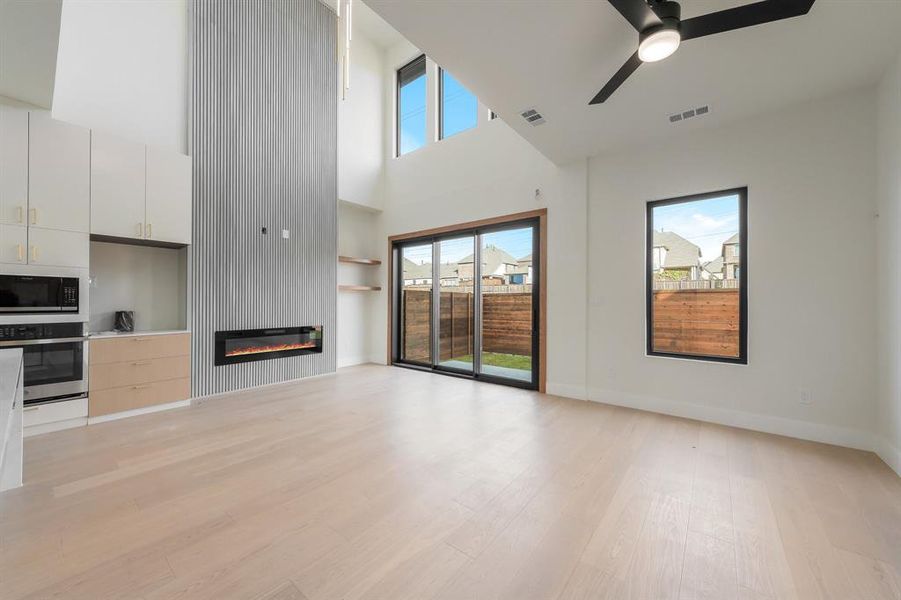 Unfurnished living room featuring a high ceiling, built in features, light wood-type flooring, a ceiling fan, and a large fireplace Unfurnished living room featuring a high ceiling, built in features, light wood-type flooring, a ceiling fan, and a large fireplace