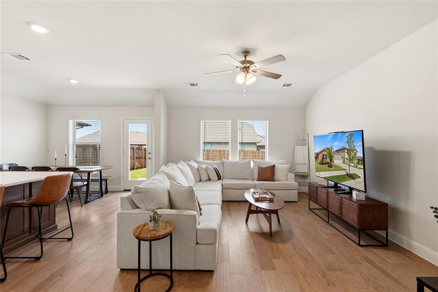 Open-concept living area with wood-finish flooring, a ceiling fan, and multiple windows
