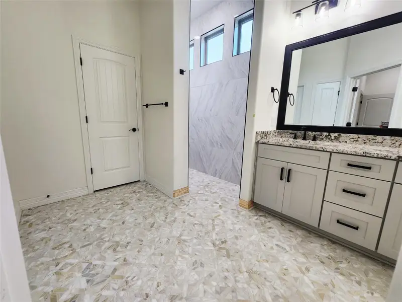 Spacious bathroom featuring patterned tile flooring, a dual-sink vanity with a light-colored countertop, and a large framed mirror with overhead lighting