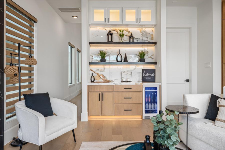 A sophisticated wet bar area with porcelain backsplash, glass-inlay cabinets, display shelves, and underlighting transforms entertaining into an art form