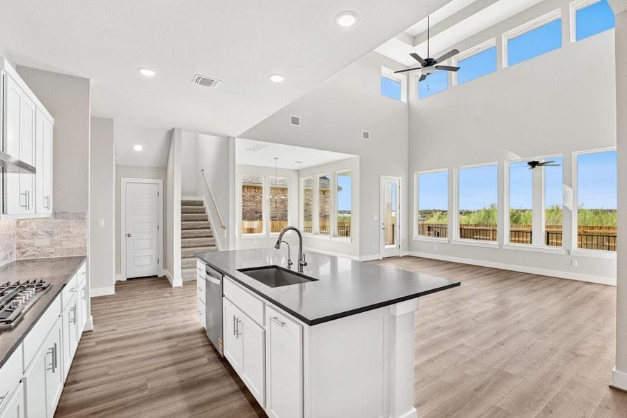 Kitchen featuring white cabinets, open floor plan, recessed lighting, light wood-style floors, and a high ceiling Kitchen featuring white cabinets, open floor plan, recessed lighting, light wood-style floors, and a high ceiling