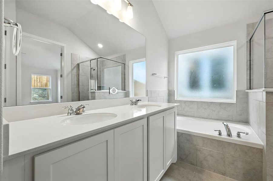 Full bathroom featuring a garden tub, lofted ceiling, double vanity, a shower stall, and dark tile patterned floors