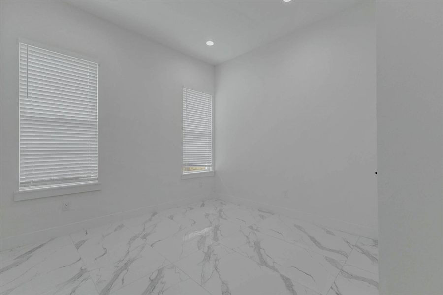 An additional bedroom view highlights the tall ceiling, large window, recessed lighting, and reflective tile flooring. The room’s clean lines and flexible proportions make it suitable for sleeping, working, exercising, or hobbies.