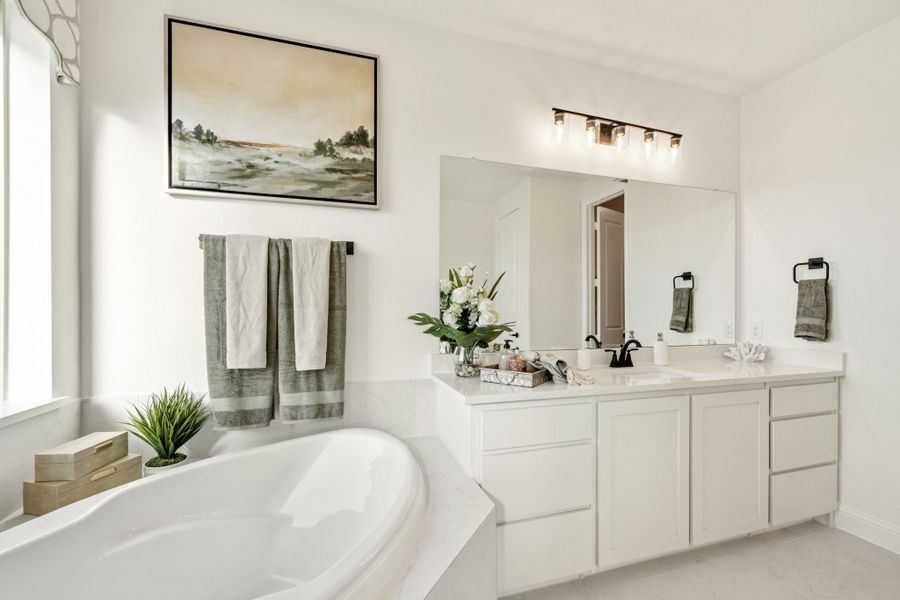 Bathroom with soaking tub, white double vanity, large mirror, and wall-mounted light fixture