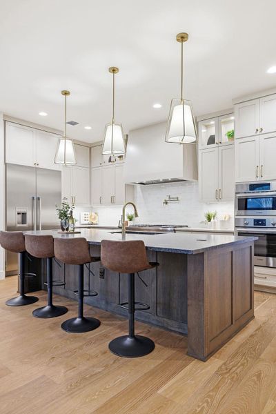Kitchen with an island with sink, white cabinets, glass insert cabinets, a breakfast bar, and recessed lighting