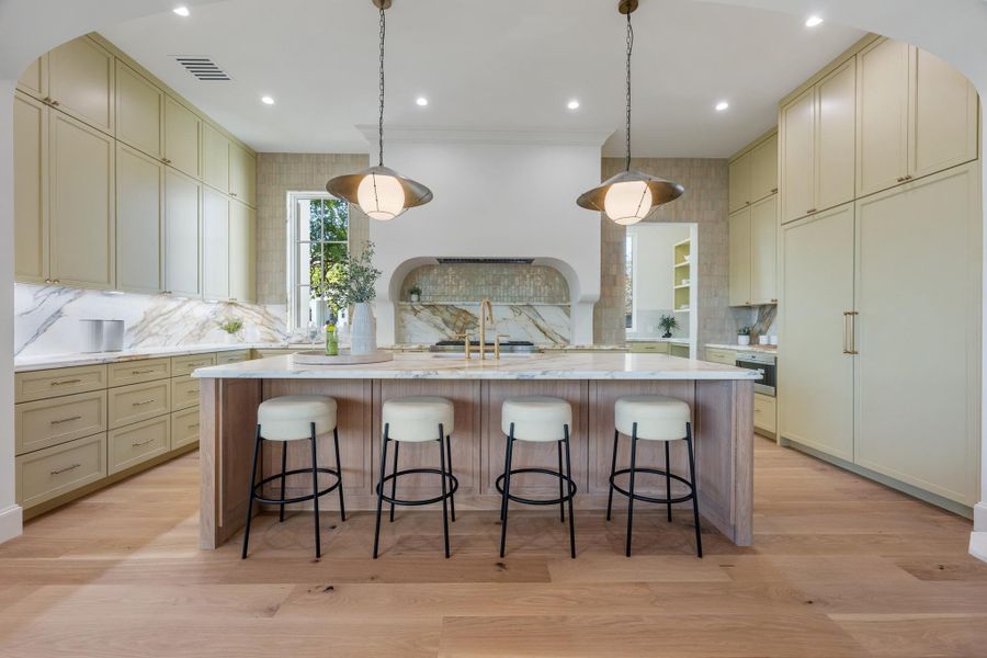Floor-to-ceiling cabinetry, a marble-topped island, and wide-plank hardwood floors anchors this custom-built kitchen space.
