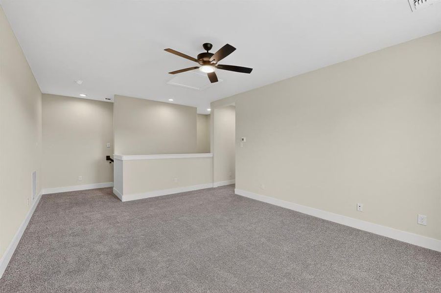 Spacious carpeted room featuring a ceiling fan, recessed lighting, and a partial wall with a railing