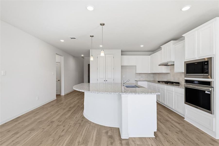Kitchen with appliances with stainless steel finishes, hanging light fixtures, white cabinets, light stone countertops, and an island with sink