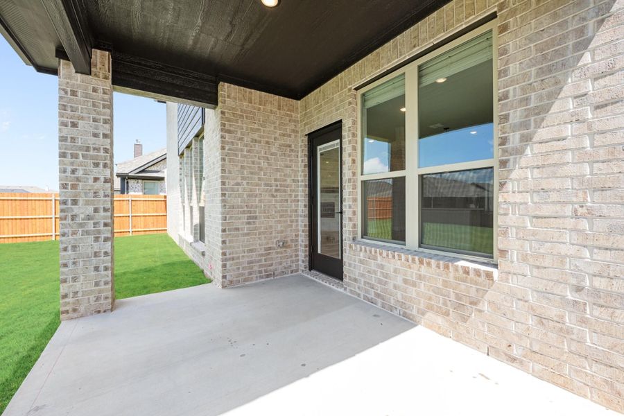 Covered back patio with concrete floor, brick exterior, black door, and fenced backyard with green lawn