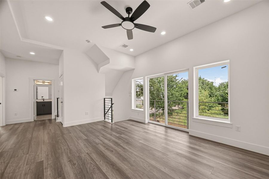 This room features modern vinyl flooring, large windows offering abundant natural light and a view of greenery, a sleek ceiling fan, and a connected bathroom. Ideal for a bright and airy living space. This room features modern vinyl flooring, large windows offering abundant natural light and a view of greenery, a sleek ceiling fan, and a connected bathroom. Ideal for a bright and airy living space.